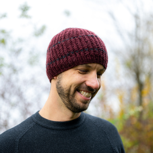 Man wearing Ambler Deven handknit men's toque in deep red with ribbed pattern and fleece headband lining.