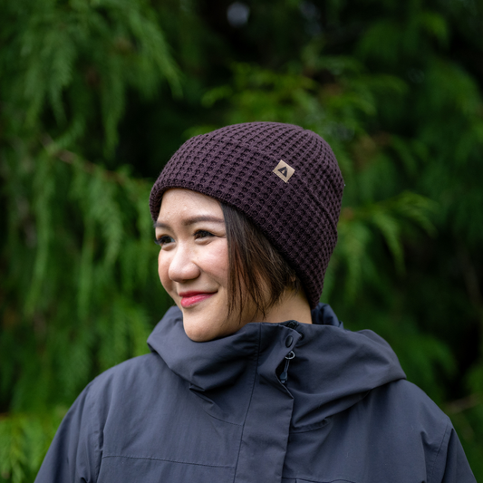 Lady wearing Made in Canada Ambler honeycomb machine knit toque in blackberry with faux leather brand clip.