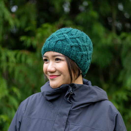 Woman wearing Ambler Kari handknit women's toque in forest with cable knit design and ribbed cuff.