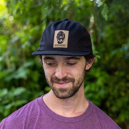 Man wearing a black snapback cap with a patch on the front panel of a bear.