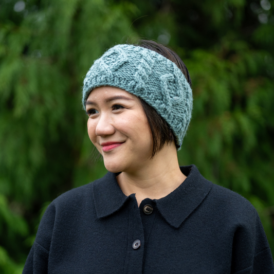 Woman wearing Ambler Mia handknit winter headband in eucalyptus with cable knit pattern and Ambler clip label.