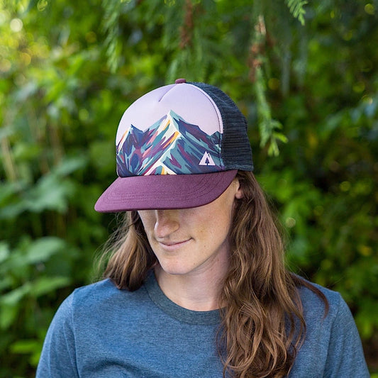 Woman wearing trucker hat with mountain design and mesh back on a white background