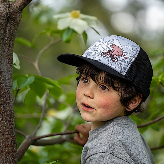 Boy wearing a kids' trucker hat with bear riding a bike design on a white background.