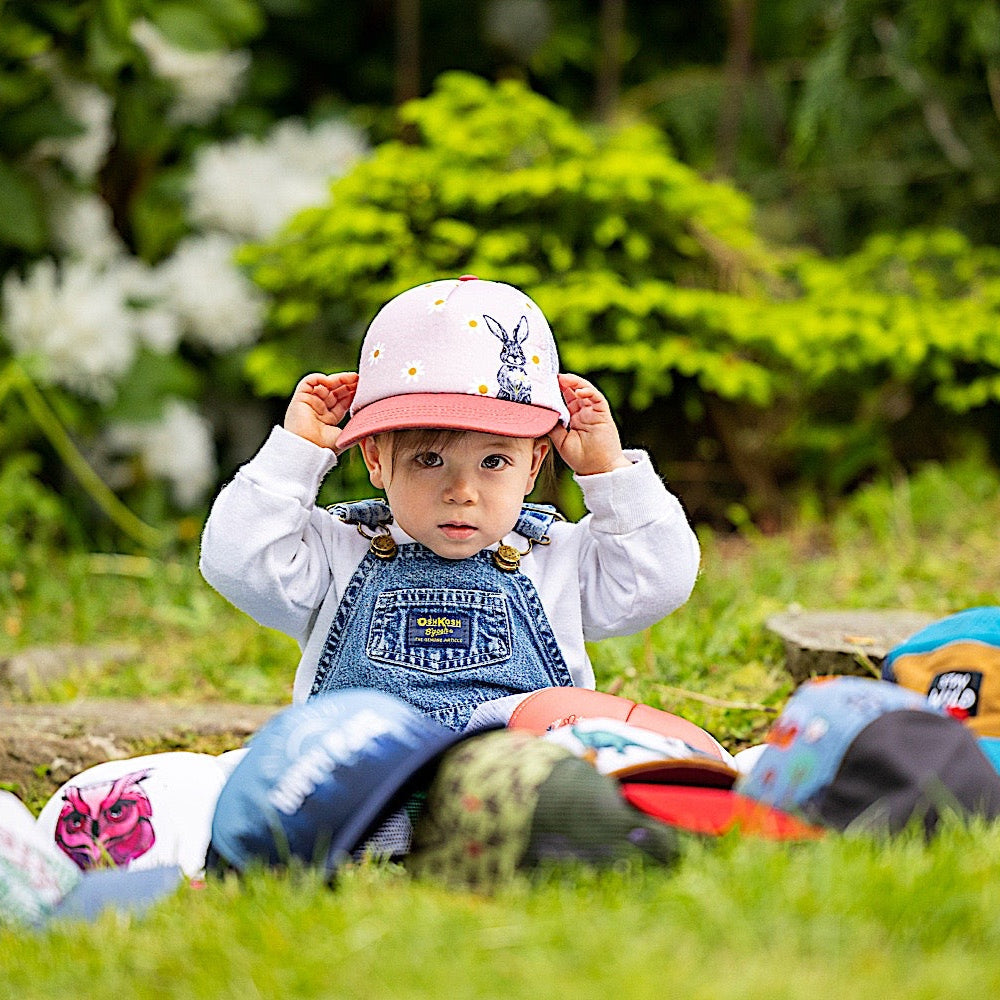 Toddler wearing pink toddler cap with a pink brim, white back and a rabbit and flower pattern on front panel.