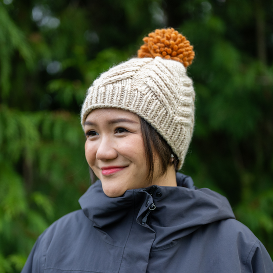 Woman wearing Ambler Audrey handknit women's toque in cream with orange medium pom.