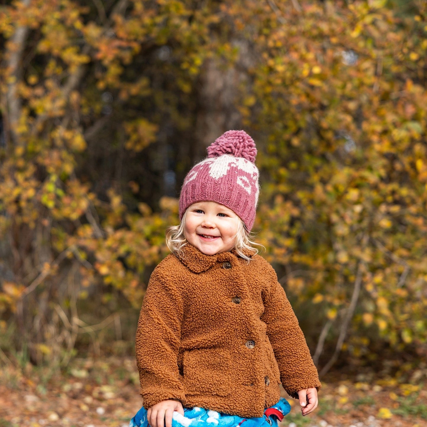 Girl wearing Ambler Bjorn handknit kids' toque in dark rose with knitted bear portrait and pom. 
