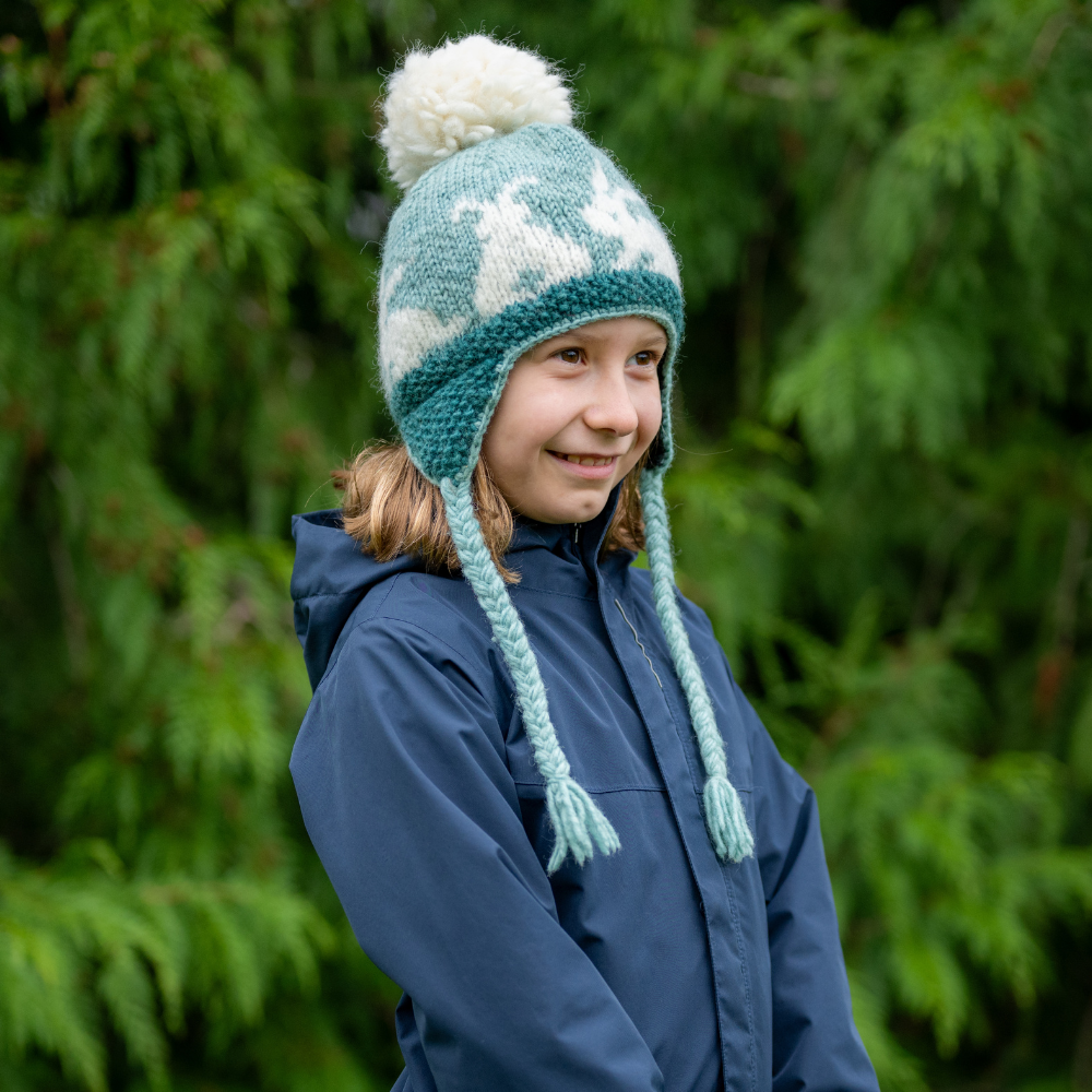 Girl wearing Ambler Bunny tales handknit kids' toque in aqua with rabbit design and coloured tassels. 