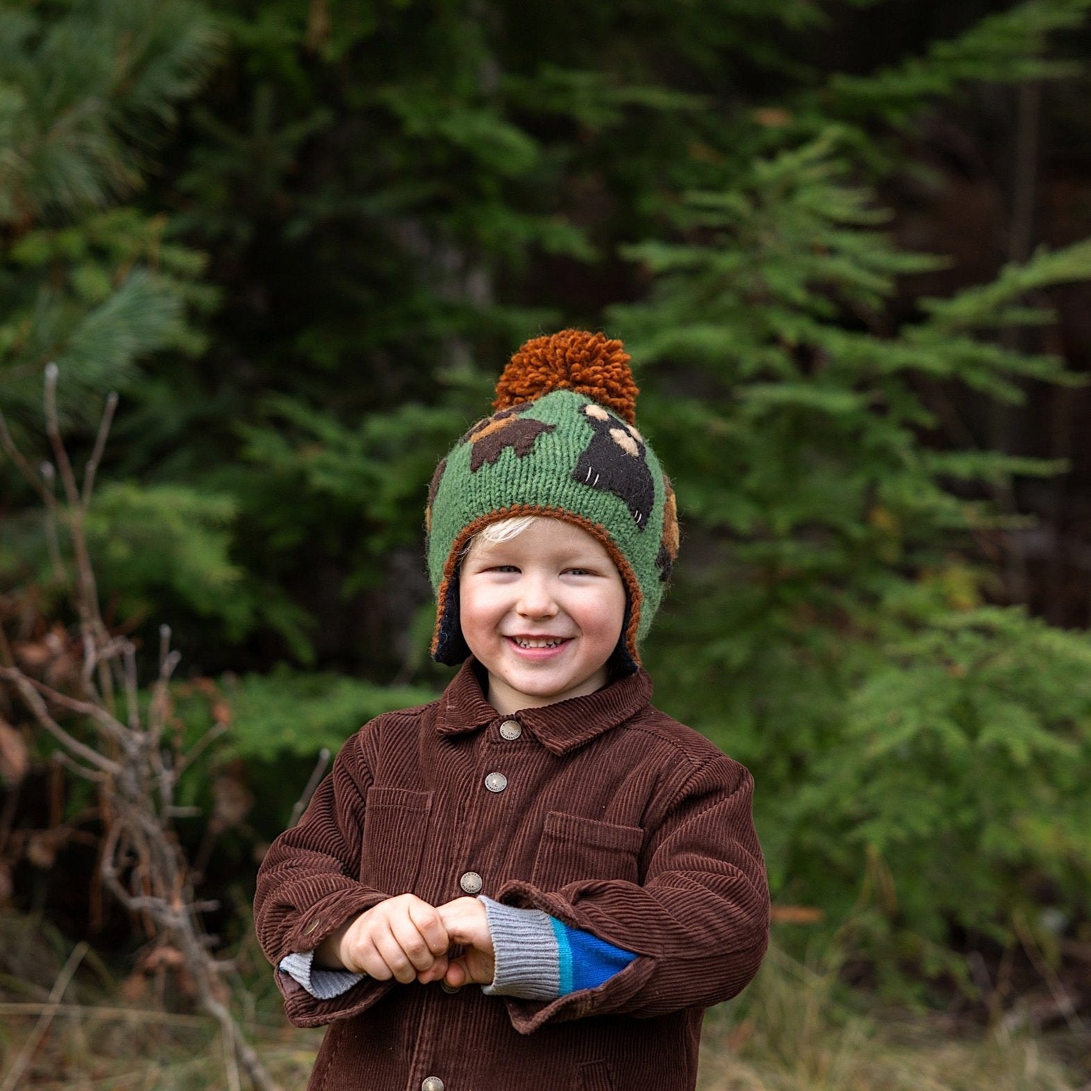 Boy wearing Ambler Canuck handknit kids' toque in green with felted creatures and medium contrast colour pom. 