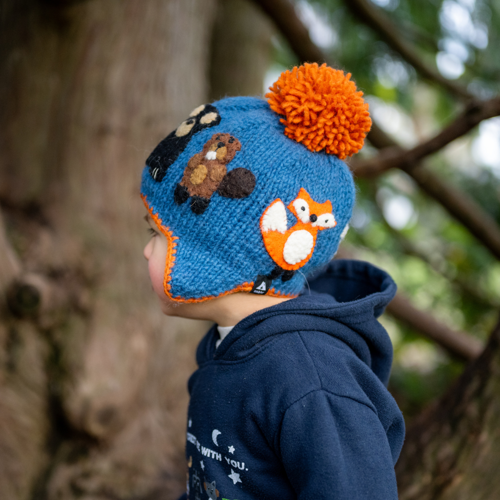 Kid wearing Ambler Canuck handknit kids' toque in dusk with felted creatures and medium contrast colour pom. 