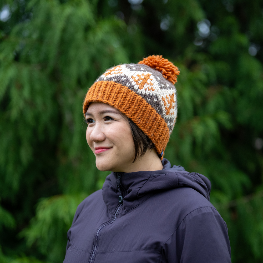 Woman wearing Ambler Cedar handknit wool toque in rust with jacquard design and medium pom. 