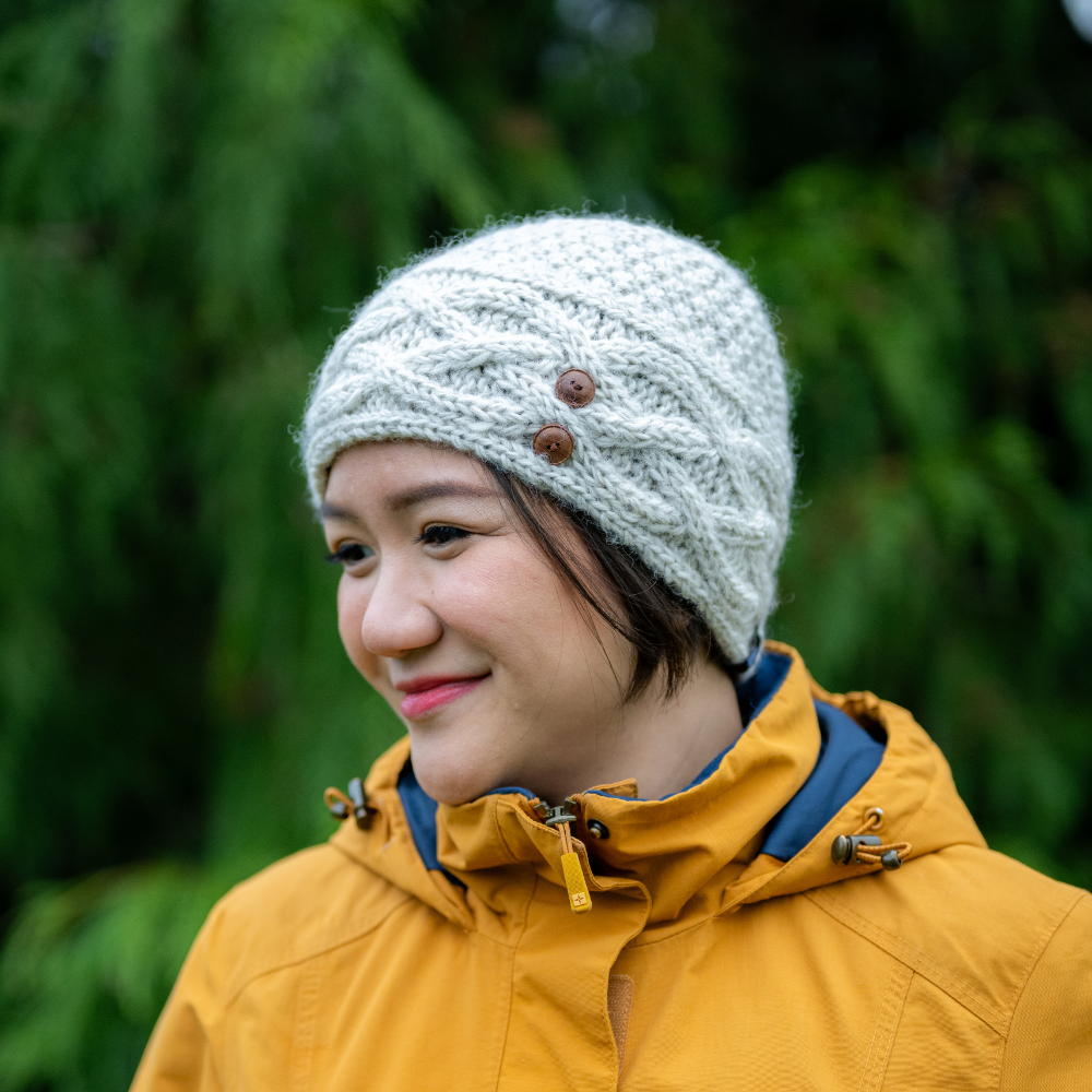 Woman wearing an Ambler Celtic handknit toque in heather stone with cable knit and buttons. 