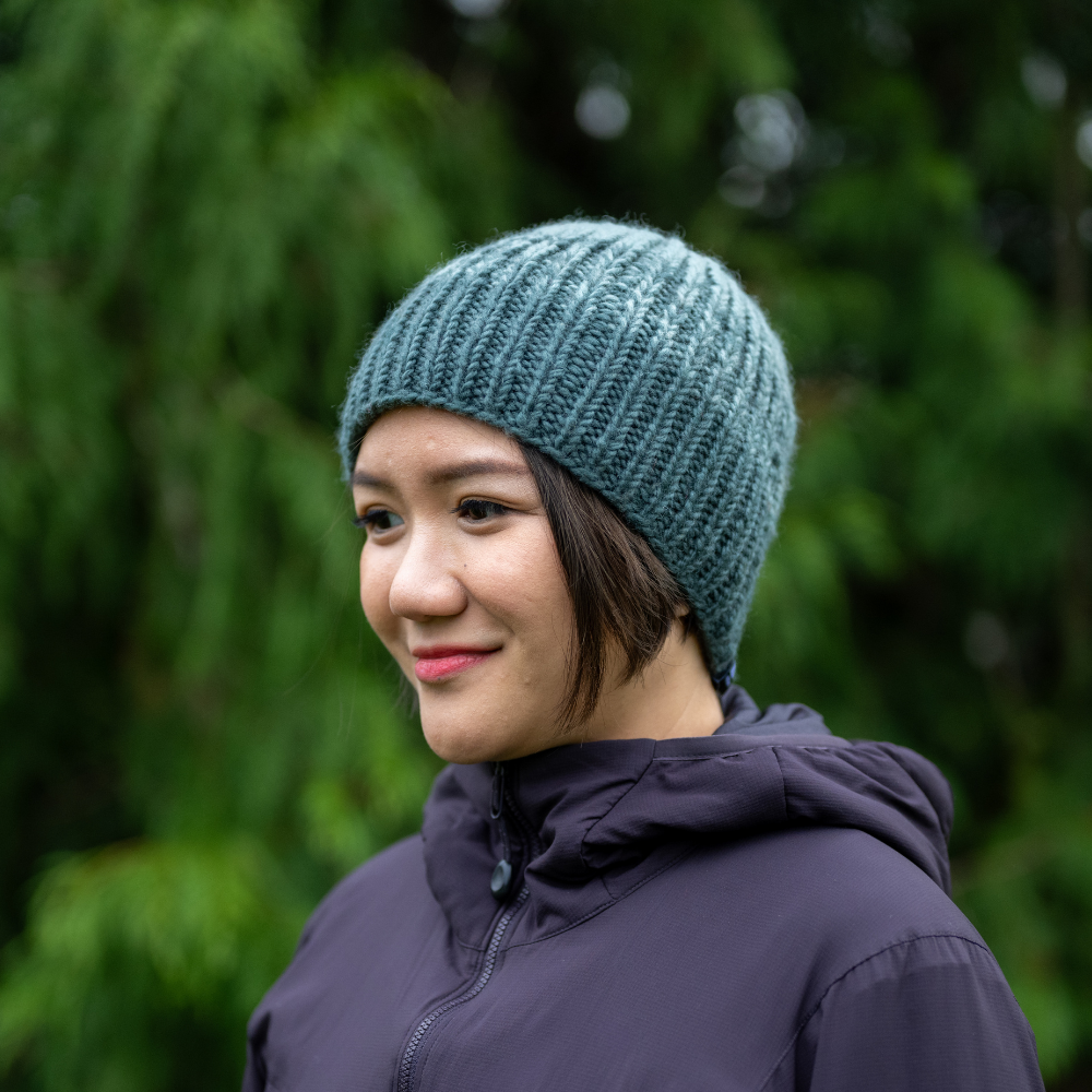 Woman wearing Ambler Cypress handknit men's toque in blue spruce with tri-colour ribbed pattern. 