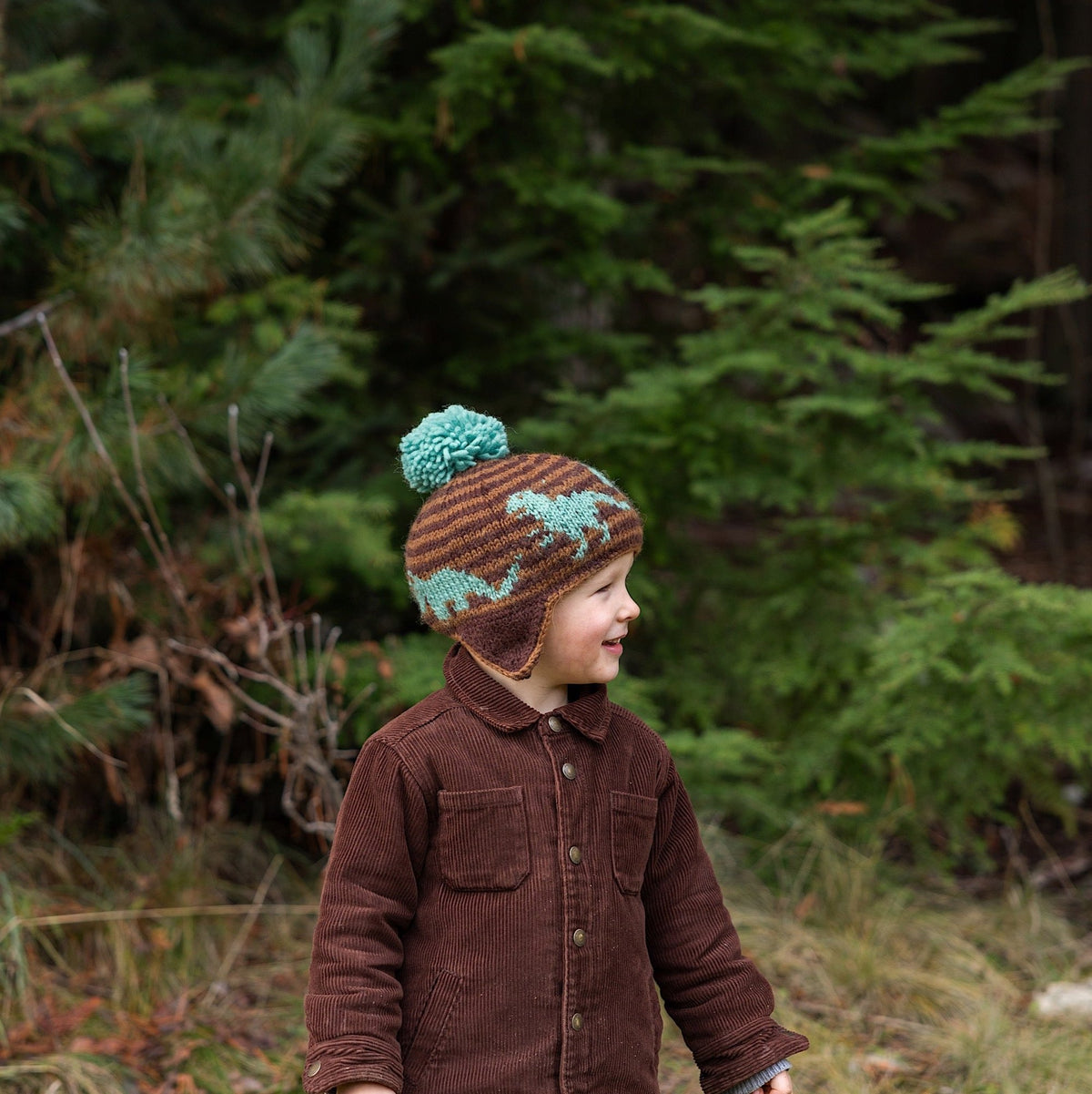 Kid wearing Ambler Dino handknit kids&#39; toque with embroidered dinosaur pattern and contrast colour pom.