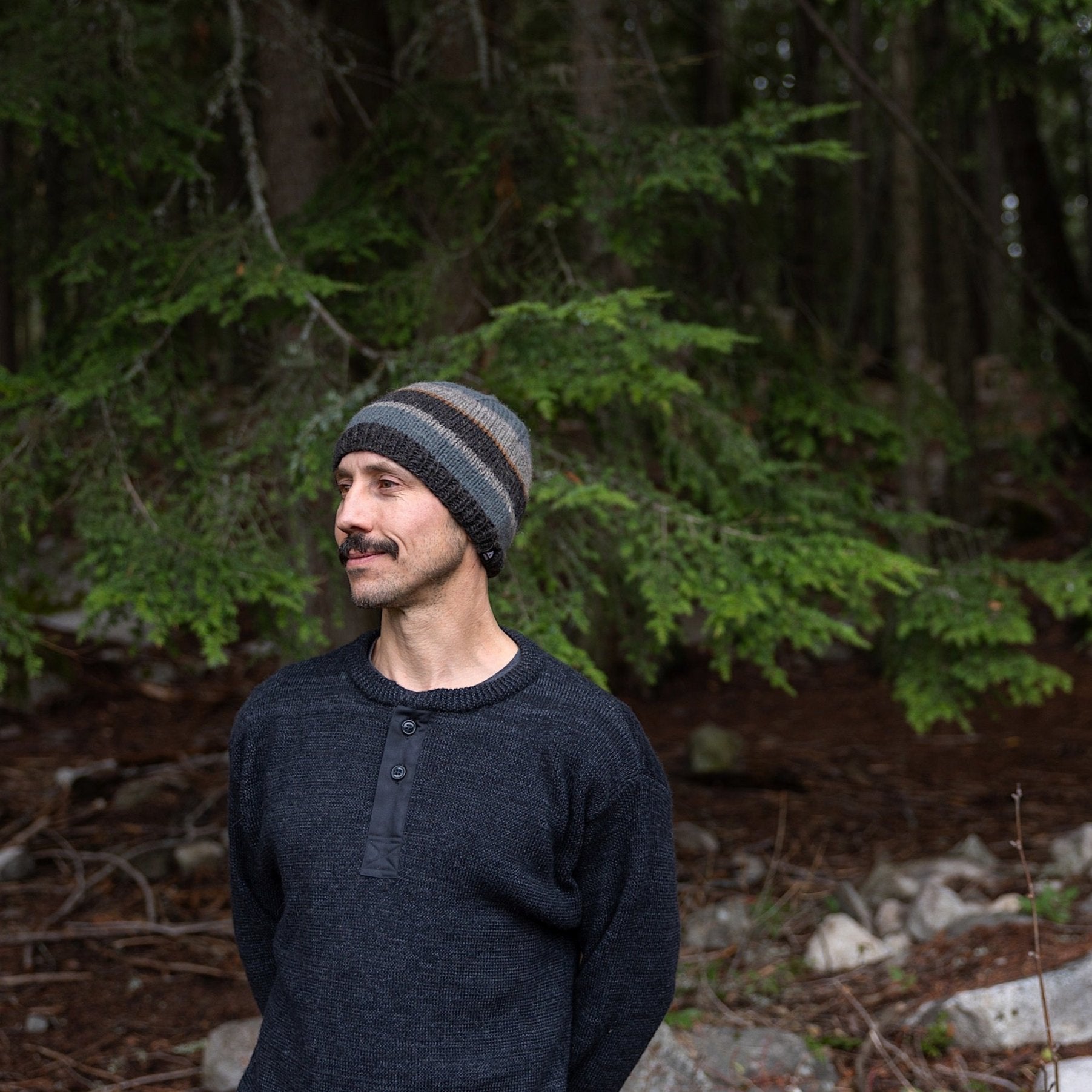 Man wearing Ambler Eric handknit wool men's toque in charcoal with tricolour striped pattern. 