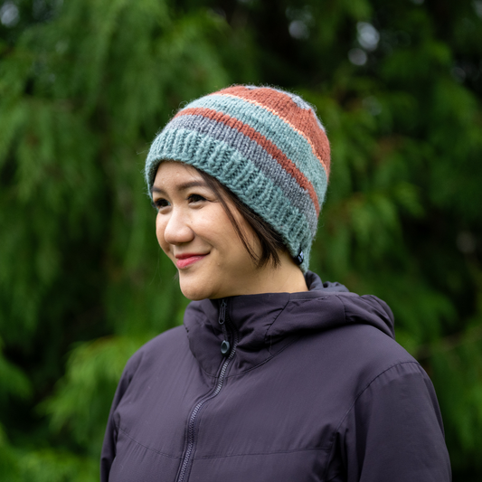 Woman wearing Ambler Eric handknit wool men's toque in eucalyptus with tricolour striped pattern. 