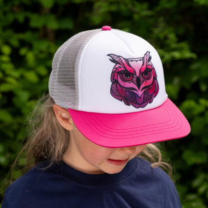 Toddler girl  wearing a trucker hat with a pink brim, white back and pink owl face design on the white front panel. 