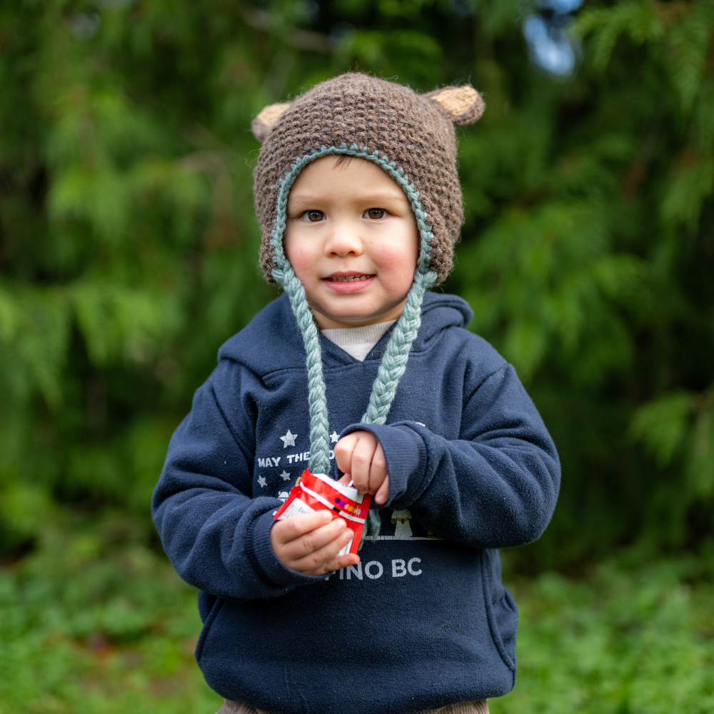Kid wearing Ambler Forest handknit kids' toque in bear with knitted bear ears and coloured tassels. 