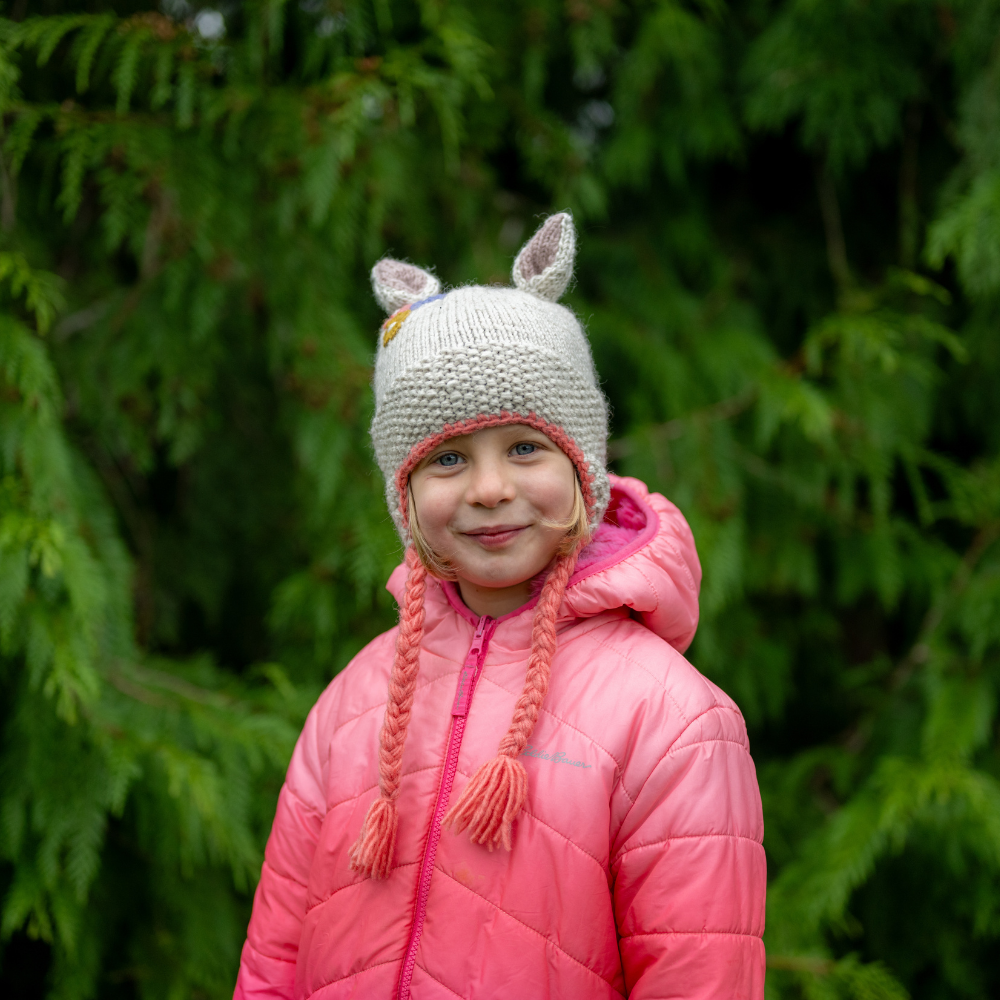Girl wearing Ambler Forest handknit kids' toque in rabbit with knitted rabbit ears and coloured tassels. 