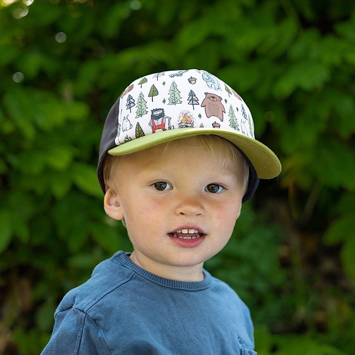 Toddler boy wearing a children's cap with green brim, grey back  and colorful lumberjack pattern on the front panel. 