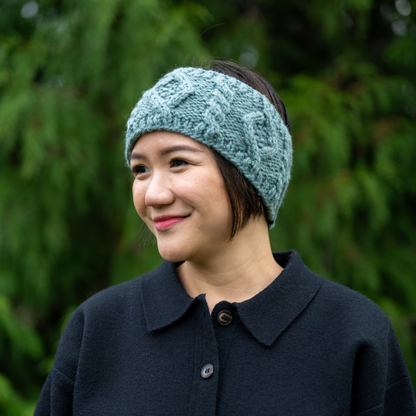Woman wearing Ambler Mia handknit winter headband in eucalyptus with cable knit pattern and Ambler clip label. 