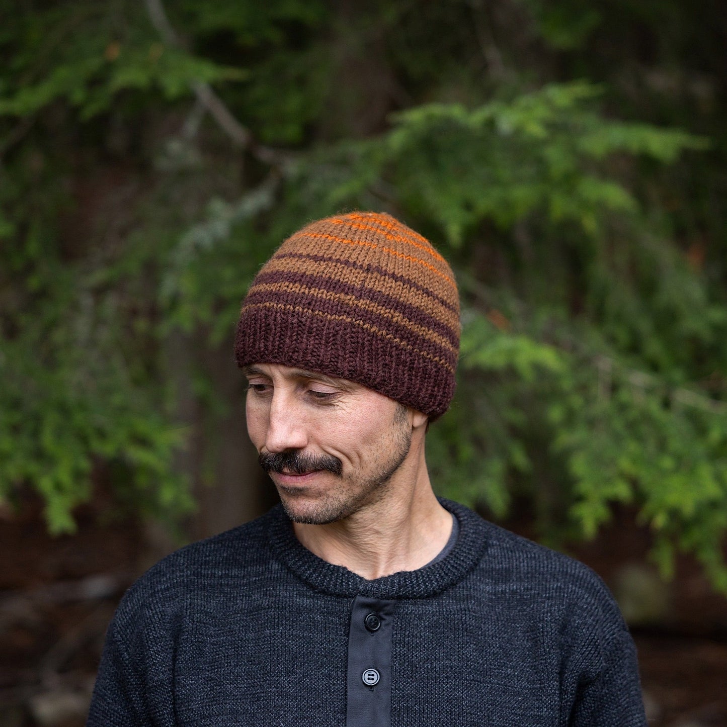 Man wearing Ambler Ollie handknit wool men's toque in espresso with striped design and warm ribbed cuff. 