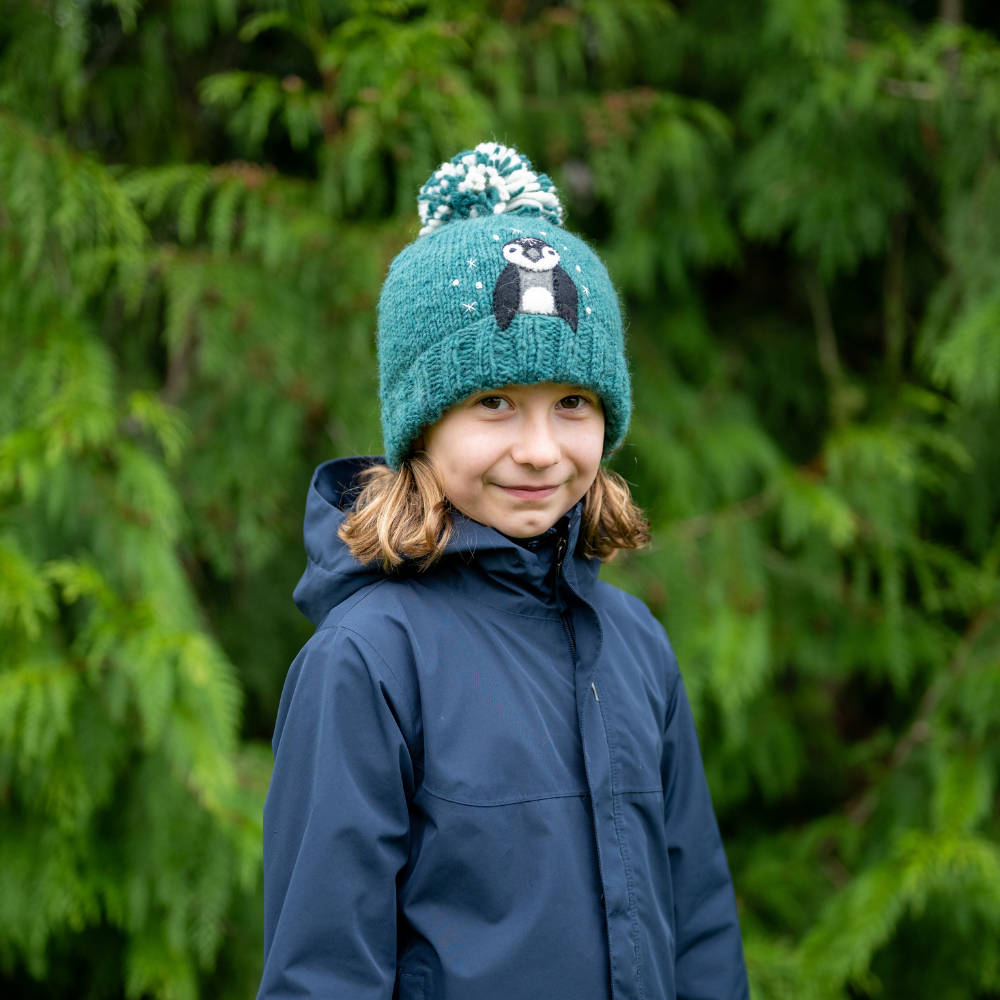 Girl wearing Ambler Peek-A-Boo handknit kids&#39; toque in teal with felted penguin character and duotone pom.