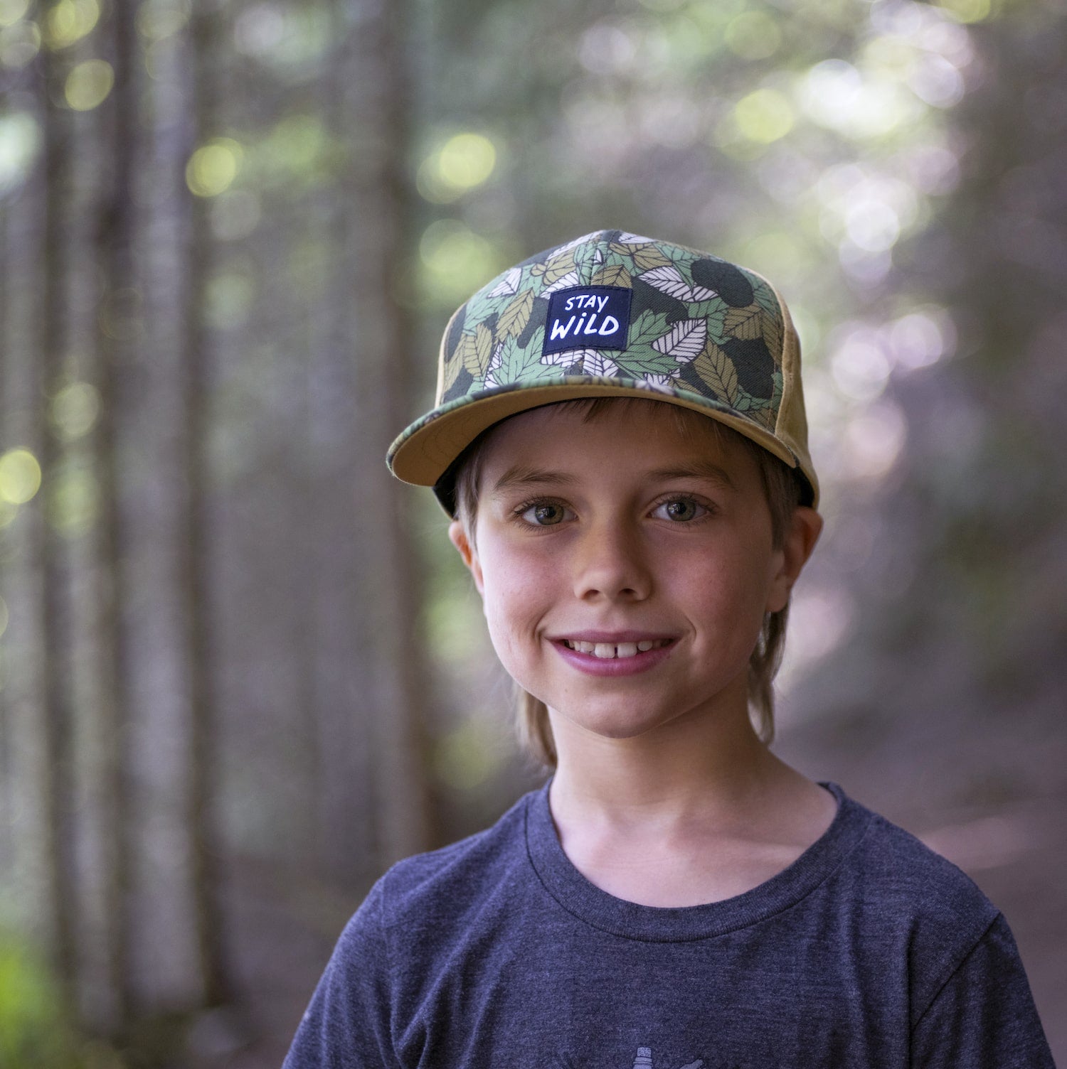 Boy wearing a kids' hat with leaf pattern and 'Stay Wild' patch on the front panel. 