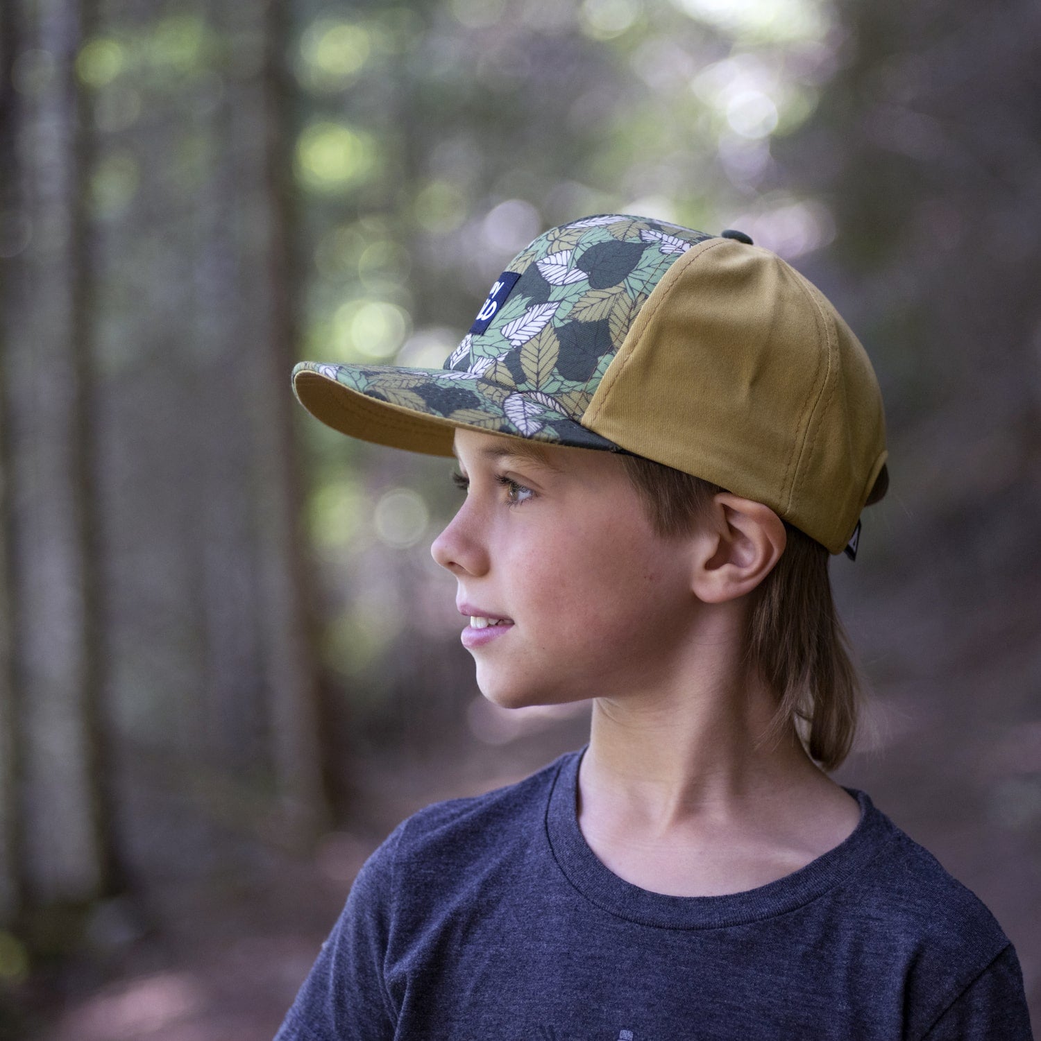 Boy wearing a kids' hat with leaf pattern and 'Stay Wild' patch on the front panel. 