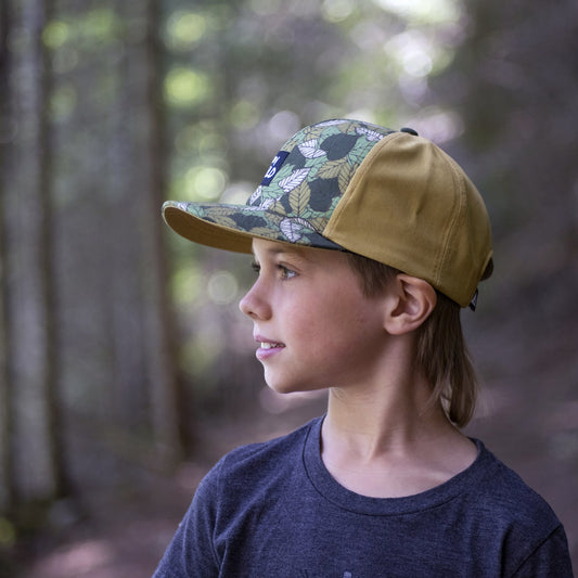 Boy wearing a kids' hat with leaf pattern and 'Stay Wild' patch on the front panel. 