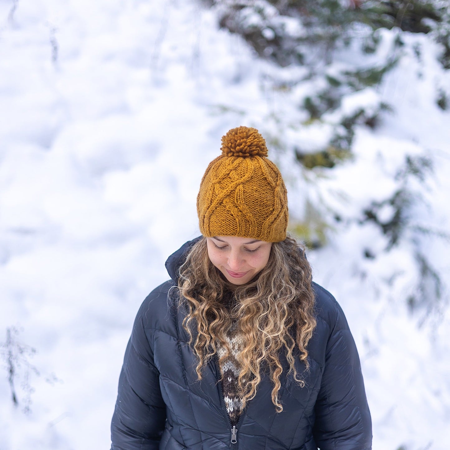 Woman wearing Ambler Tracks handknit wool women's toque in bronze with cable knit pattern and medium pom. 