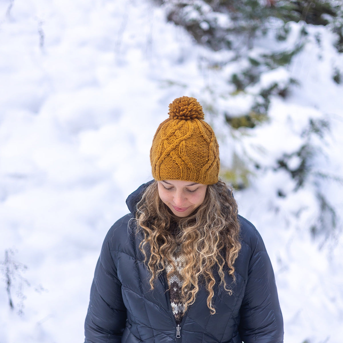 Woman wearing Ambler Tracks handknit wool women&#39;s toque in bronze with cable knit pattern and medium pom. 
