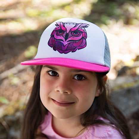 Girl wearing a kid&#39;s trucker hat with a pink brim, white back and pink owl face design on the white front panel. 