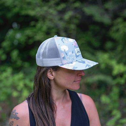 Woman wearing a floral-patterned trucker hat with an Ambler brand logo on a white background. 