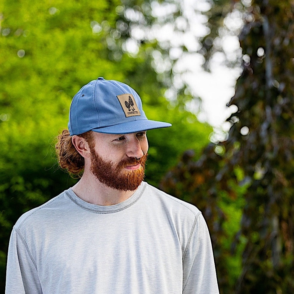 Man wearing slate blue snapback cap with a patch on the front panel. 