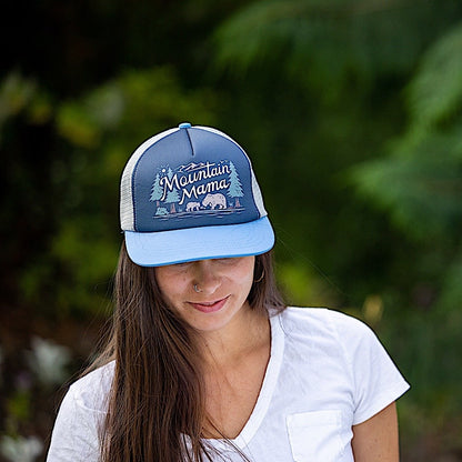 Woman wearing a blue trucker hat with 'Mountain Mama' graphic design on the front panel. 