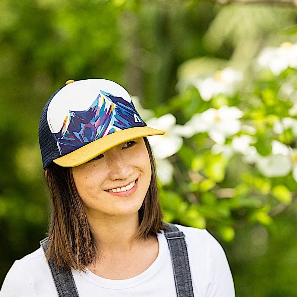 Woman wearing trucker hat with mountain design and mesh back on a white background